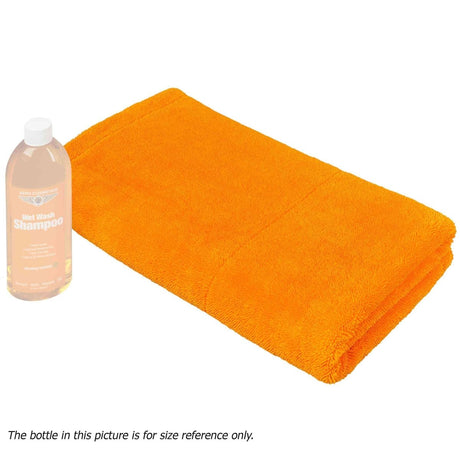 A large orange microfiber towel is displayed next to a bottle, which is used for scale reference. The towel appears to be soft and fluffy, indicating high absorbency.
